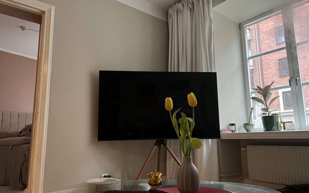 Ett foto på ett vardagsrum med en stor tv i bakgrunden och en vas med gula tulpaner i förgrunden